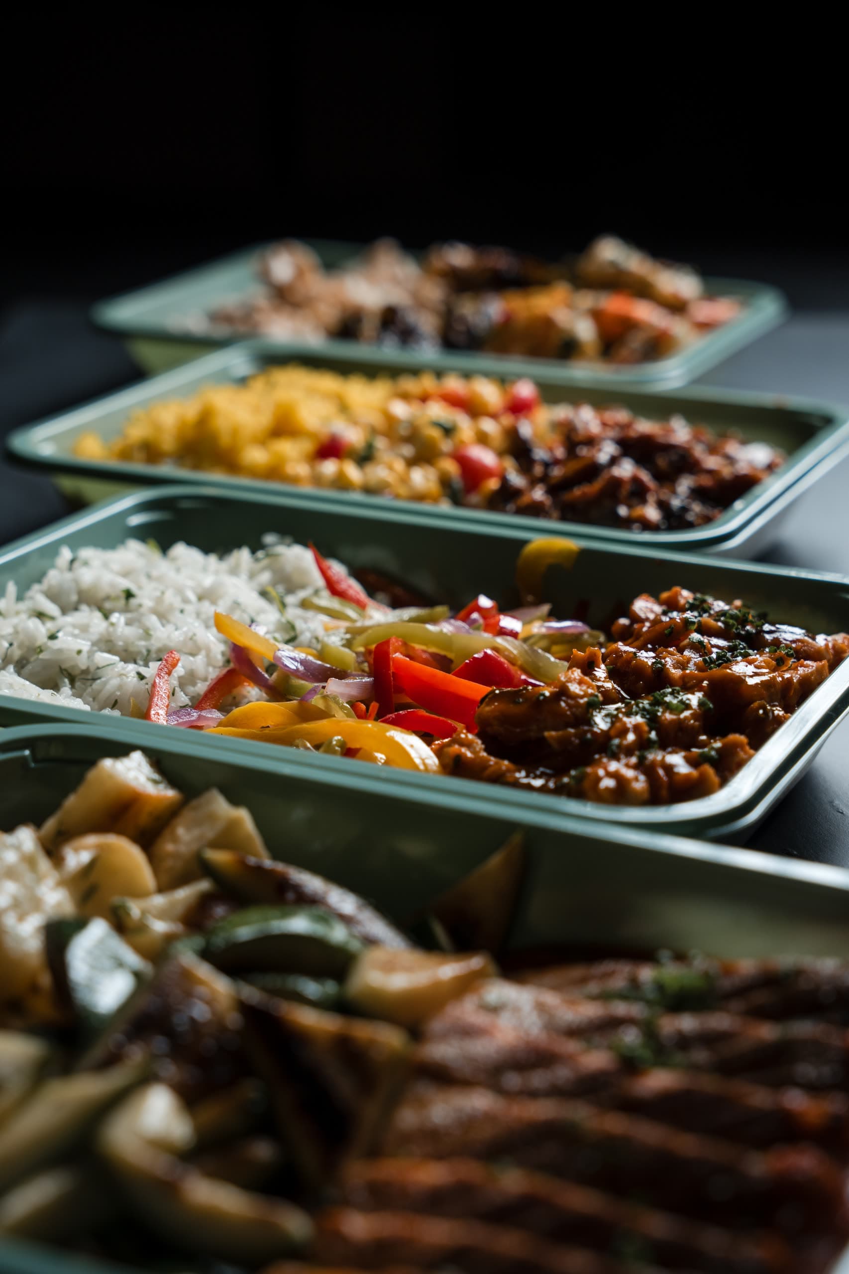 Four trays of ABLTY meals in a receding line, herbed rice, sautéed peppers and braised chicken sharp in the tray at centre